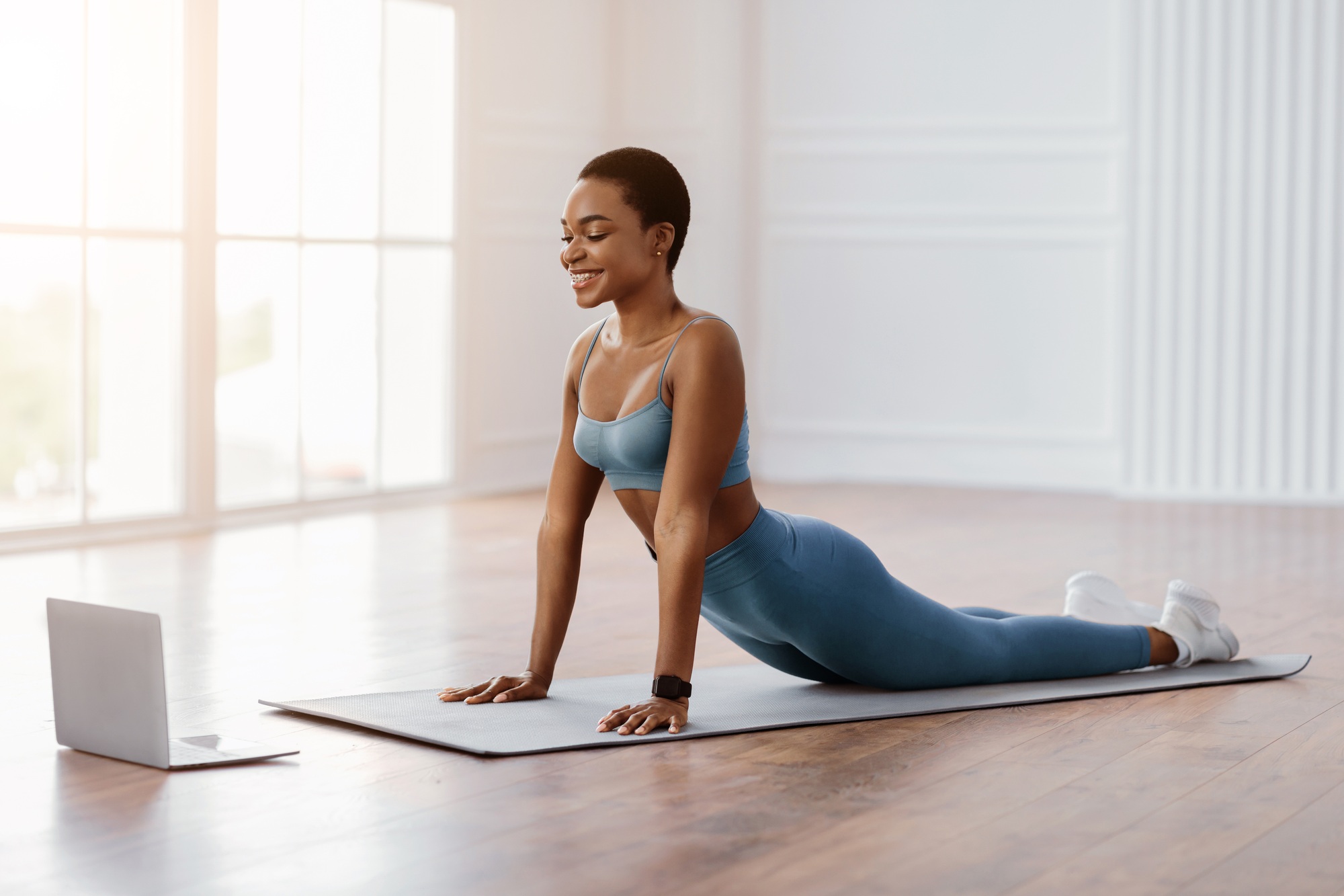 Young african woman stretching back on mat with pc